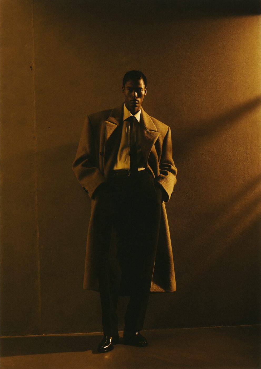 AI-generated fashion editorial: model in a camel wool coat against an amber-lit wall